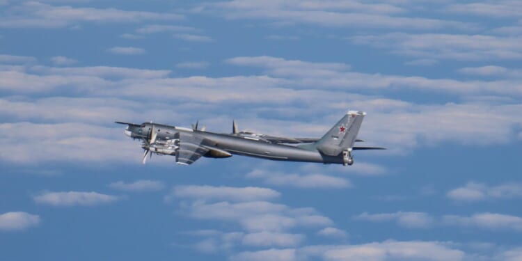 A Russian Tu-95 bomber aircraft in flight against a cloudy sky.