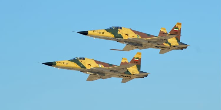 Two Iranian F-5 fighter jets flying against a blue sky.