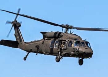 A UH-60 Black Hawk helicopter with US Army markings flying in a blue sky.