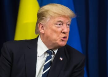 Trump sitting in front of a Ukrainian flag.