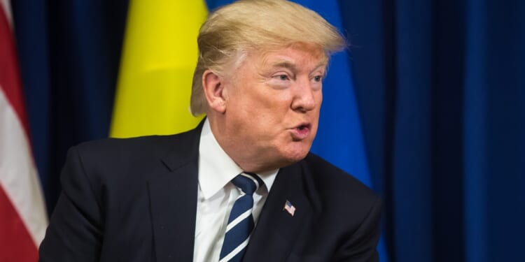 Trump sitting in front of a Ukrainian flag.