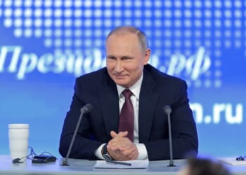 Russian President Vladimir Putin smiling at a press conference.