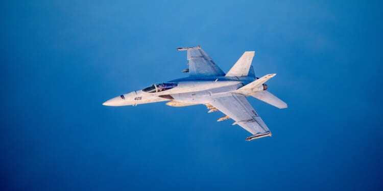 An F/A-18 Super Hornet in flight against a blue backdrop.