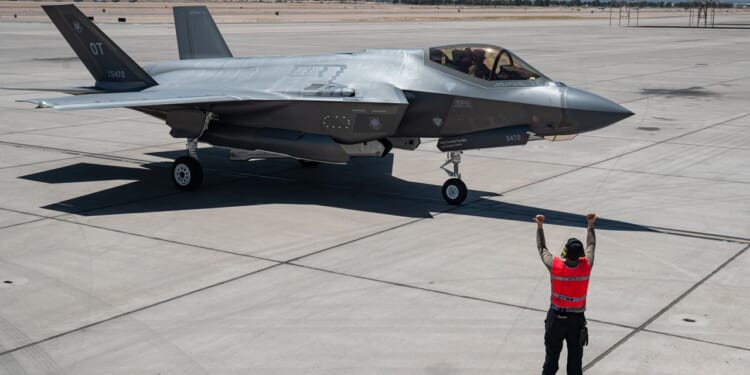 An aircraft marshal guides an F-35 fighter jet on the tarmac.