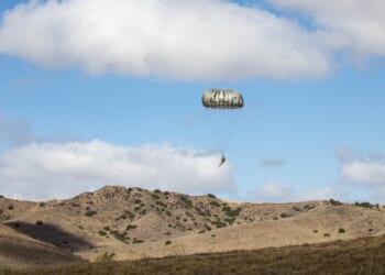 A US soldier landing on the ground with a parachute.