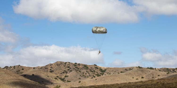A US soldier landing on the ground with a parachute.