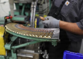 A worker putting rifle ammunition together at a factory.