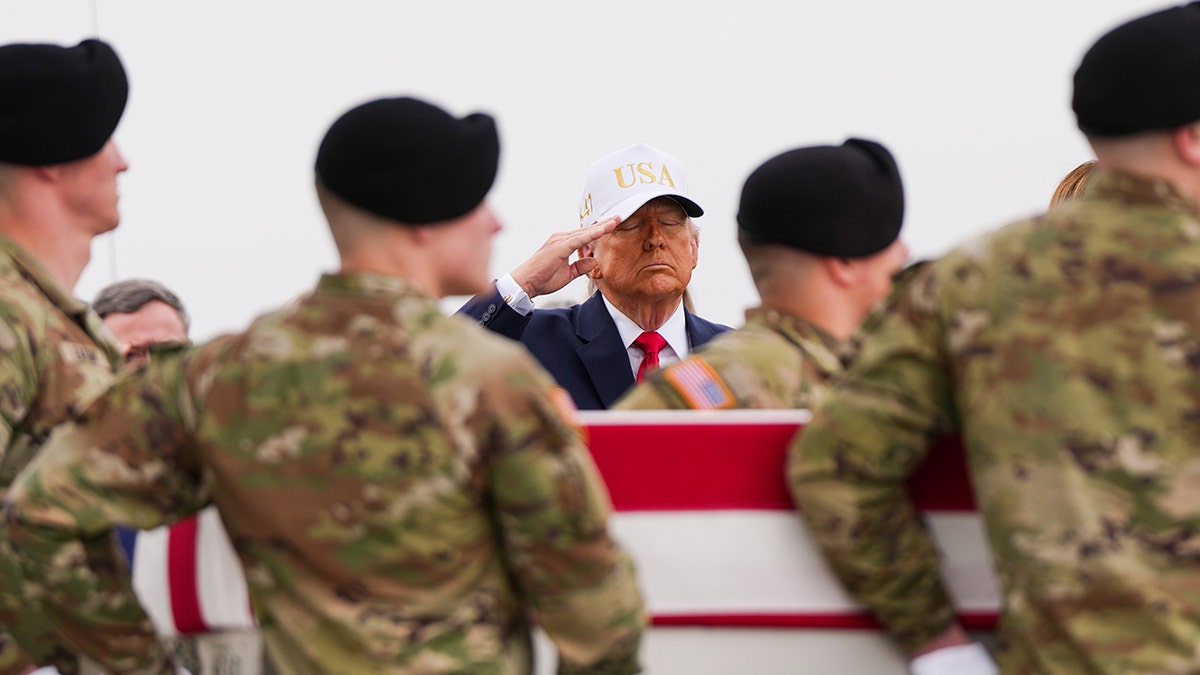Donald Trump saluting as an Army carry team moves a flag-draped transfer case at Dover Air Force Base.