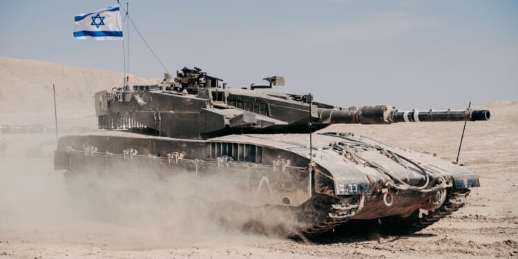 An tank in the desert flies an Israeli flag and kicks up dust.
