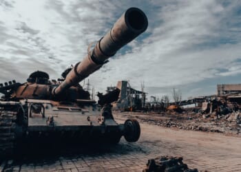 A damaged tank on display near a ruined building.