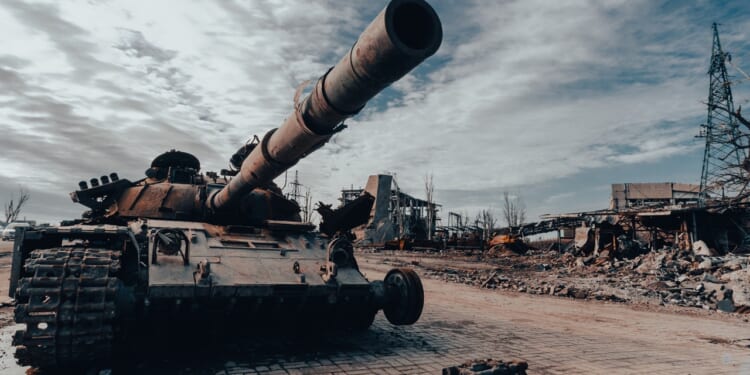 A damaged tank on display near a ruined building.