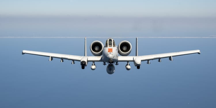 An A-10 Warthog in flight over a blue body of water.