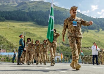 A group of Pakistani soldiers marching under a Pakistani flag.