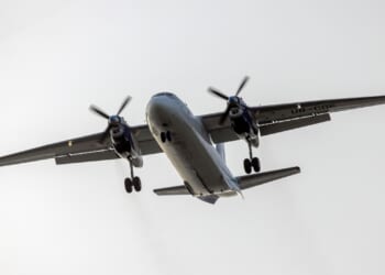 An Antonov An-26 propeller aircraft in flight against a cloudy sky.