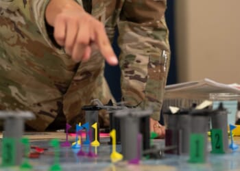 A soldier points at a wargame in progress on a tabletop.