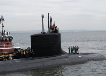 The USS New Jersey submarine at sea, accompanied by a tugboat.