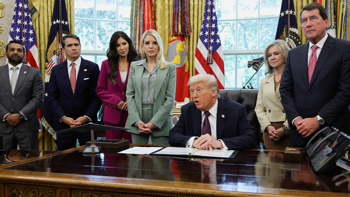 President Donald Trump signing a memorandum in the Oval Office with officials including FBI Director Kash Patel
