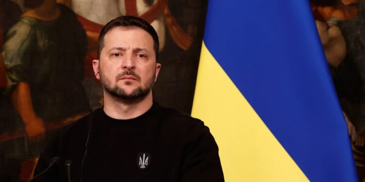 President Volodymyr Zelensky speaks in front of a Ukrainian flag.